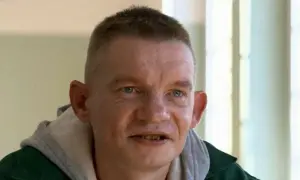 Mężczyzna z krótkimi włosami i niebieskimi oczami, ubrany w zieloną kurtkę i szary kaptur. Wygląda jakby miał zarost, a jego usta są lekko otwarte. Może to nasz bandziorek?