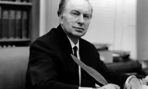 L. Ron Hubbard, twórca scjentologii, siedzi przy biurku z piórem w dłoni, gotów do pisania.