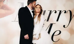 Ben Affleck całuje w czoło Jennifer Lopez, która w białej sukni trzyma torebkę. Para wygląda na zakochanych.
