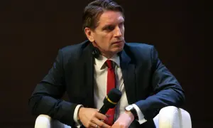 Tomasz Lis w garniturze i czerwonym krawacie, z mikrofonem w dłoni. Mówi o swojej chorobie.