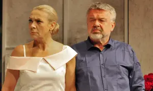 Kobieta w białej sukni i mężczyzna w granatowej koszuli patrzą w bok z zamyślonymi minami.