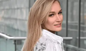 Uśmiechnięta Kamila Boś, w białej koszuli z wzorem, patrzy przez ramię.