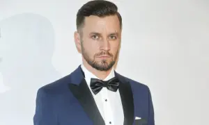 Piotr Domalewski w granatowym garniturze i czarnej muszce. Wygląda jakby właśnie wracał do żony po ważnym wydarzeniu.