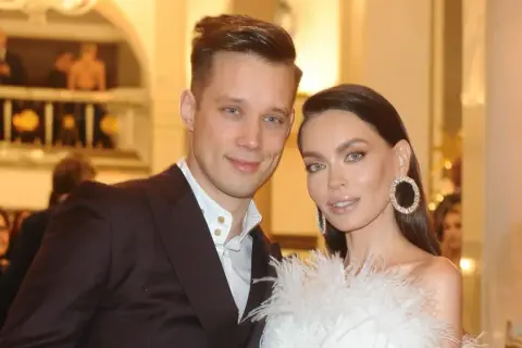 Edyta Zając z partnerem na eleganckim wydarzeniu. Ona w białej kreacji z piórami i błyszczącymi kolczykami, on w garniturze.