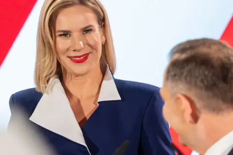 Pierwsza dama Polski, uśmiechnięta, w granatowej marynarce z białym kołnierzem, podczas oficjalnego wydarzenia.