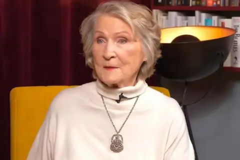 Irena Santor nie żyje. Ikona polskiej piosenki, w białym golfie i z naszyjnikiem, siedzi na żółtym fotelu.
