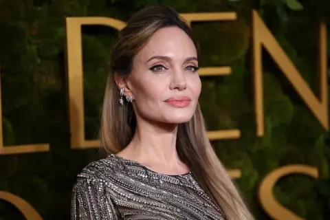 Angelina Jolie, jedna z najbardziej znanych aktorek Hollywood, w błyszczącej kreacji na tle złotych liter.