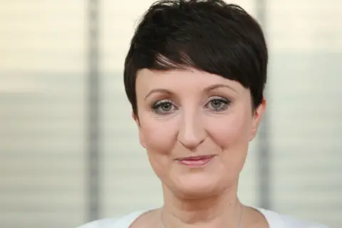 Agnieszka Burzyńska zmagająca się z chorobą, patrzy w obiektyw z delikatnym uśmiechem.