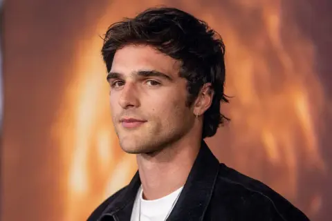 Jacob Elordi, którego dziewczyna może być zazdrosna o jego urok, pozuje na tle ognistego krajobrazu.
