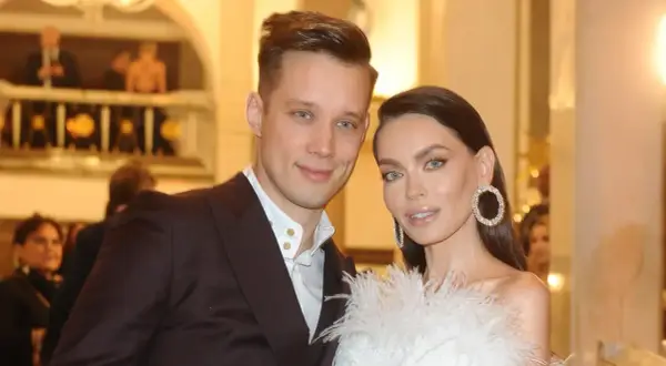 Edyta Zając z partnerem na eleganckim wydarzeniu. Ona w białej kreacji z piórami i błyszczącymi kolczykami, on w garniturze.