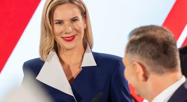Pierwsza dama Polski, uśmiechnięta, w granatowej marynarce z białym kołnierzem, podczas oficjalnego wydarzenia.