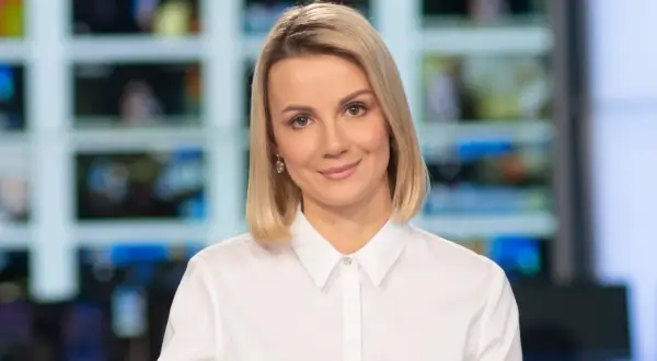 Joanna Dunikowska-Paź, znana z Wikipedii, w białej koszuli, z kolczykami, na tle ekranów.