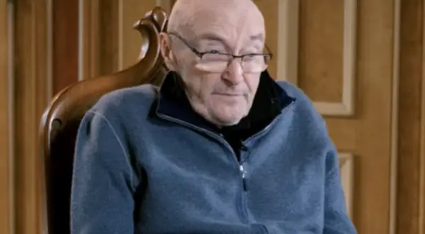 Phil Collins, zmagający się z chorobą, siedzi w fotelu, ubrany w niebieski polar.