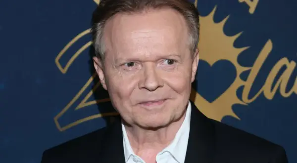 Michał Bajor w czarnym garniturze i białej koszuli, z uśmiechem na twarzy. Choć nie widać jego żony, jego spojrzenie zdaje się mówić o szczęściu.
