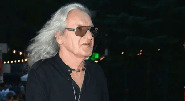 Grzegorz Markowski z długimi siwymi włosami i w okularach przeciwsłonecznych, w czarnej koszuli. W tle widać światła i tłum ludzi.