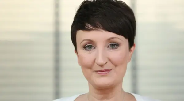 Agnieszka Burzyńska zmagająca się z chorobą, patrzy w obiektyw z delikatnym uśmiechem.