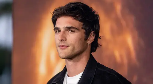 Jacob Elordi, którego dziewczyna może być zazdrosna o jego urok, pozuje na tle ognistego krajobrazu.