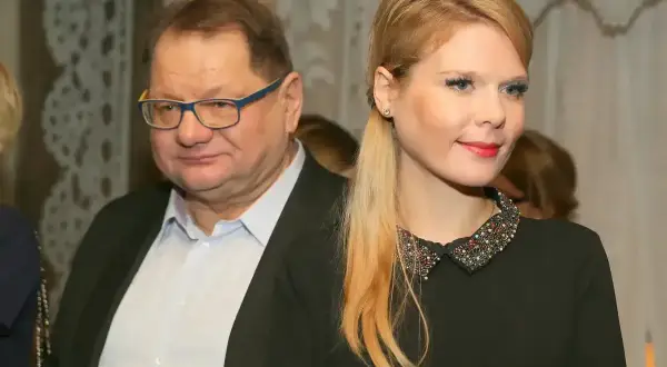 Mężczyzna w okularach i jego żona, ubrana w czarną sukienkę z ozdobnym kołnierzykiem, pozują do zdjęcia.