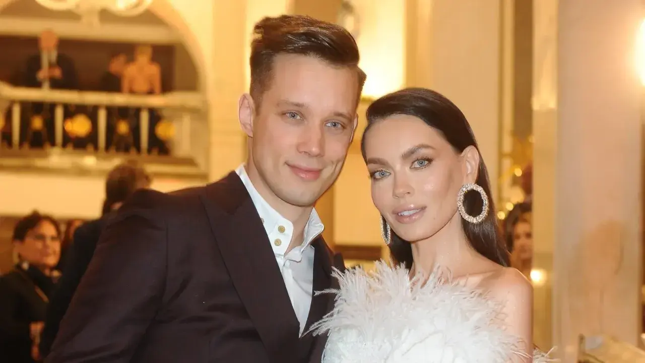 Edyta Zając z partnerem na eleganckim wydarzeniu. Ona w białej kreacji z piórami i błyszczącymi kolczykami, on w garniturze.