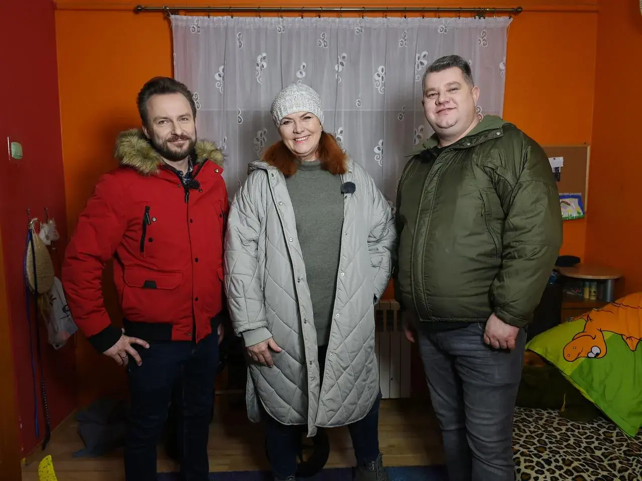 Trzy osoby stoją w pokoju. Mężczyzna w czerwonej kurtce, kobieta w szarej i mężczyzna w zielonej. To nasz nowy dom, Arek nie żyje.