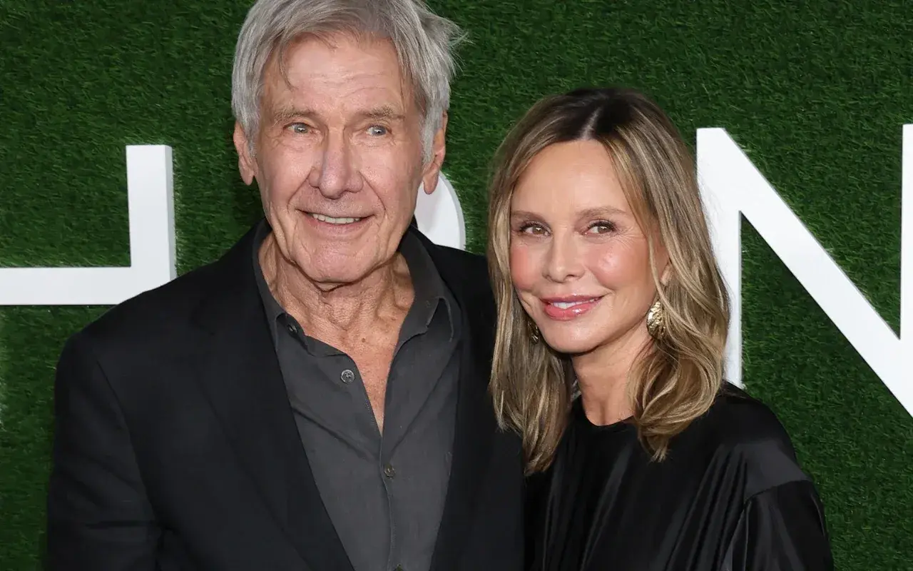Harrison Ford i jego żona Calista Flockhart uśmiechają się do aparatu na tle zielonej ściany z białymi literami.