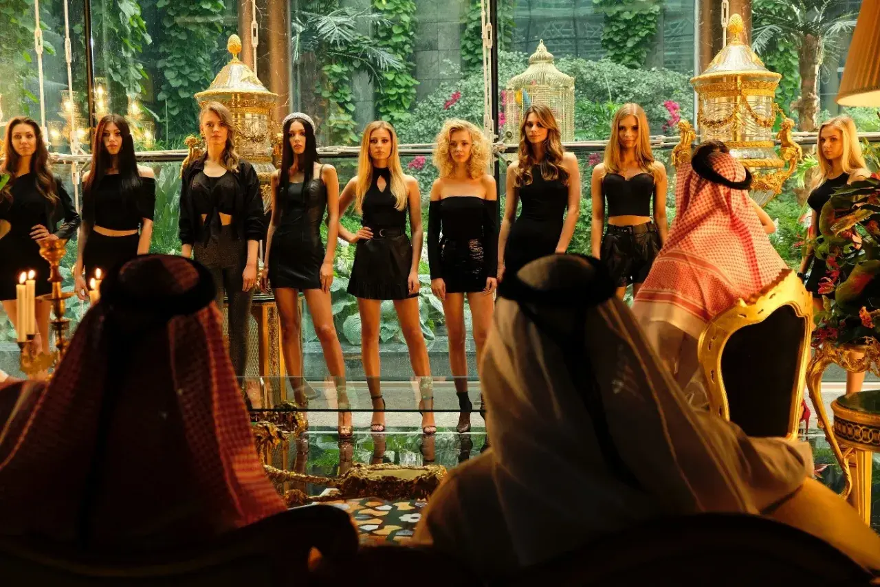 Scena przypominająca aferę dubajską: mężczyźni w tradycyjnych strojach obserwują grupę kobiet w czarnych sukienkach.