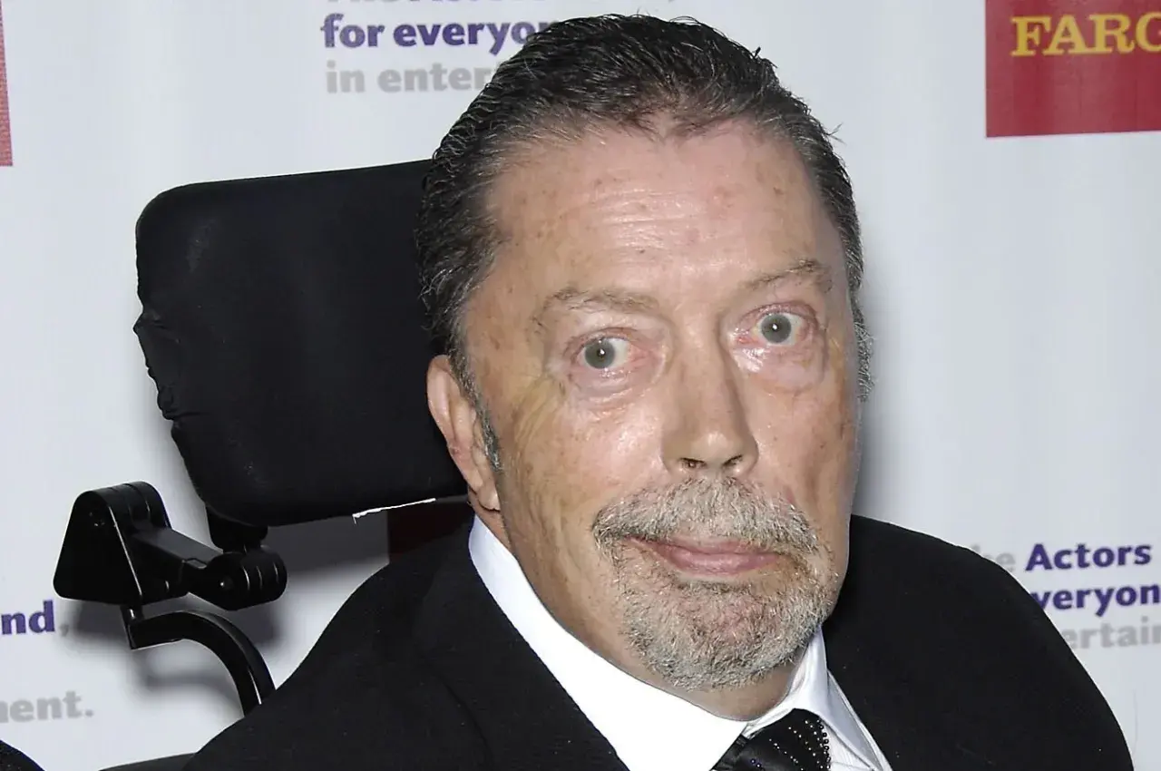 Tim Curry w wózku inwalidzkim, zmagający się z chorobą, ale wciąż z iskrą w oku.