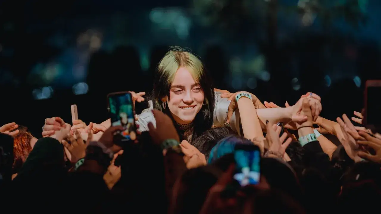 Uśmiechnięta Billie Eilish w tłumie fanów, którzy chcą dotknąć swojej idolki. Jej utwory poruszają serca wielu.