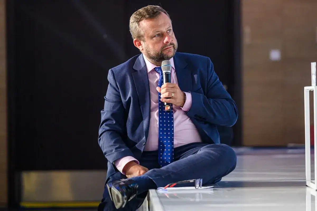 Adrian Klarenbach w garniturze, trzymający mikrofon, opowiada o swojej chorobie.