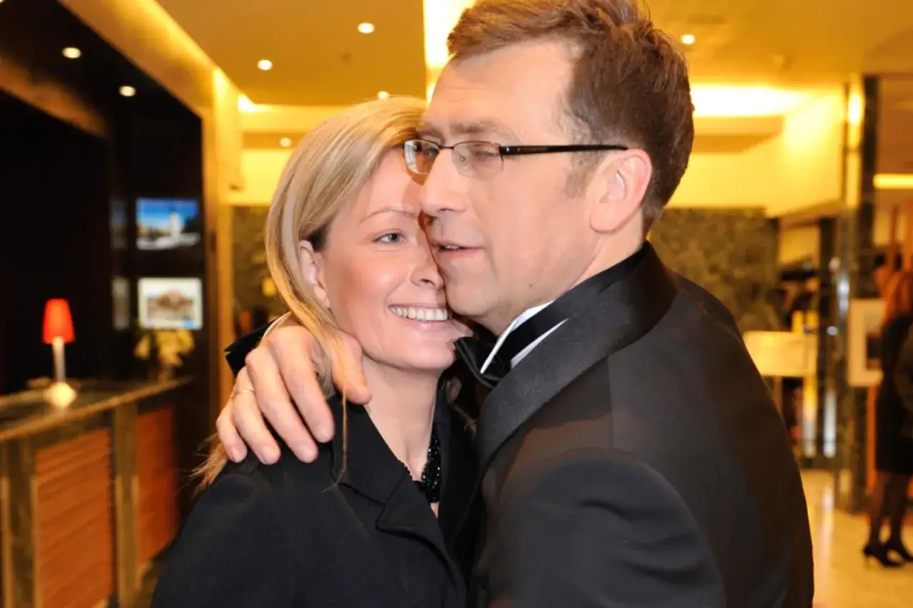 Maciej Orłoś obejmuje swoją żonę, oboje uśmiechnięci.