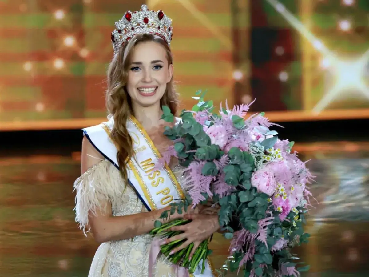 Uśmiechnięta Miss Polski z koroną i bukietem różowych kwiatów.