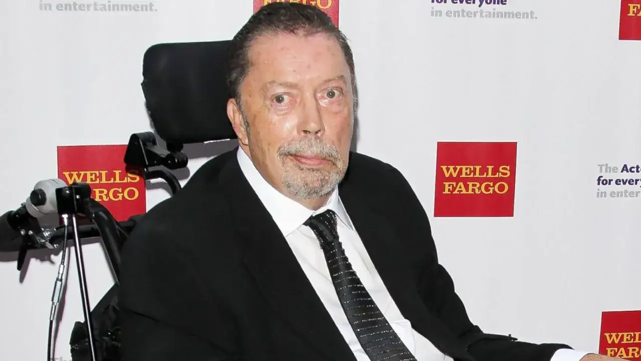 Tim Curry w wózku inwalidzkim, zmagający się z chorobą, ale wciąż z charakterystycznym spojrzeniem.