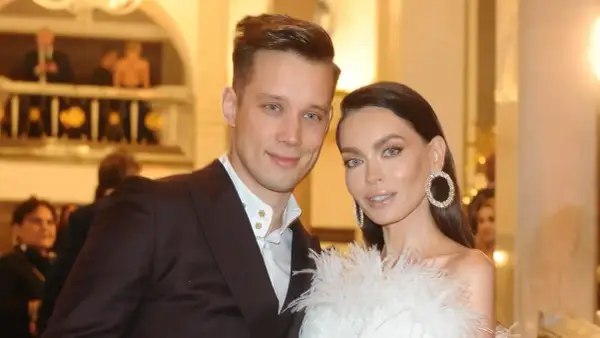 Edyta Zając z partnerem na eleganckim wydarzeniu. Ona w białej kreacji z piórami i błyszczącymi kolczykami, on w garniturze.