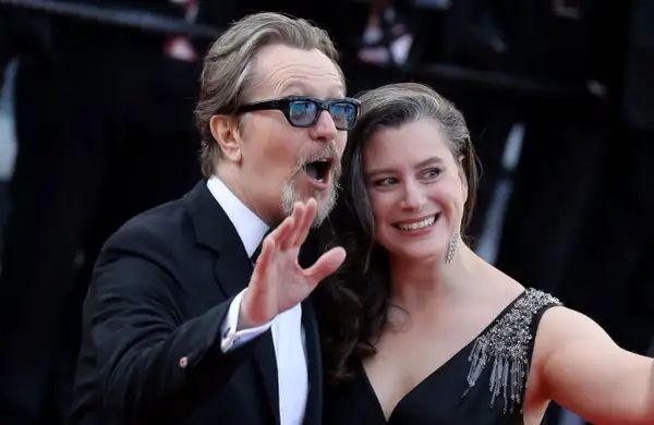 Gary Oldman z żoną, uśmiechnięci i pełni życia, pozują do zdjęć na czerwonym dywanie.