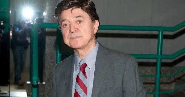 Jerzy Połomski w szarym garniturze i krawacie, otoczony przez błyski fleszy.