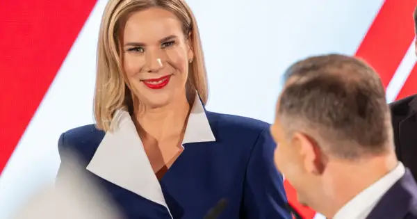 Pierwsza dama Polski, uśmiechnięta, w granatowej marynarce z białym kołnierzem, podczas oficjalnego wydarzenia.