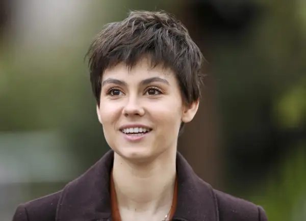Uśmiechnięta Pola Gonciarz, w brązowym płaszczu, wygląda jakby właśnie usłyszała coś zabawnego od swojego partnera.