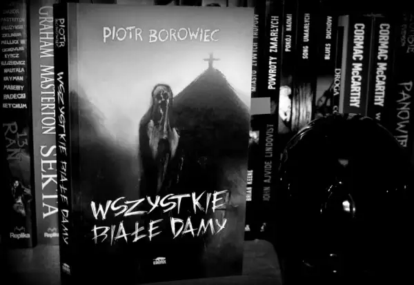 Czarno-biała okładka książki "Wszystkie białe damy" Piotra Borowca z postacią i krzyżem.