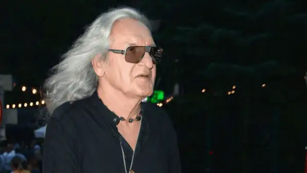 Grzegorz Markowski z długimi siwymi włosami i w okularach przeciwsłonecznych, w czarnej koszuli. W tle widać światła i tłum ludzi.