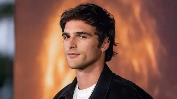 Jacob Elordi, którego dziewczyna może być zazdrosna o jego urok, pozuje na tle ognistego krajobrazu.